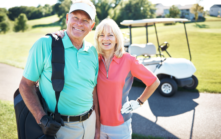 Older woman with arm around husband, both smiling, posing on golf course with golf cart in background